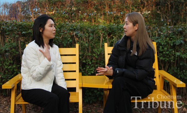 Two young women talking to each other on yellow chairs at Pureun-gil Park